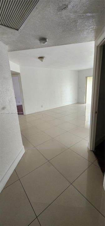 Large-format neutral tile flooring throughout an open-concept area featuring smooth white walls and overhead flush-mount lighting fixtures
