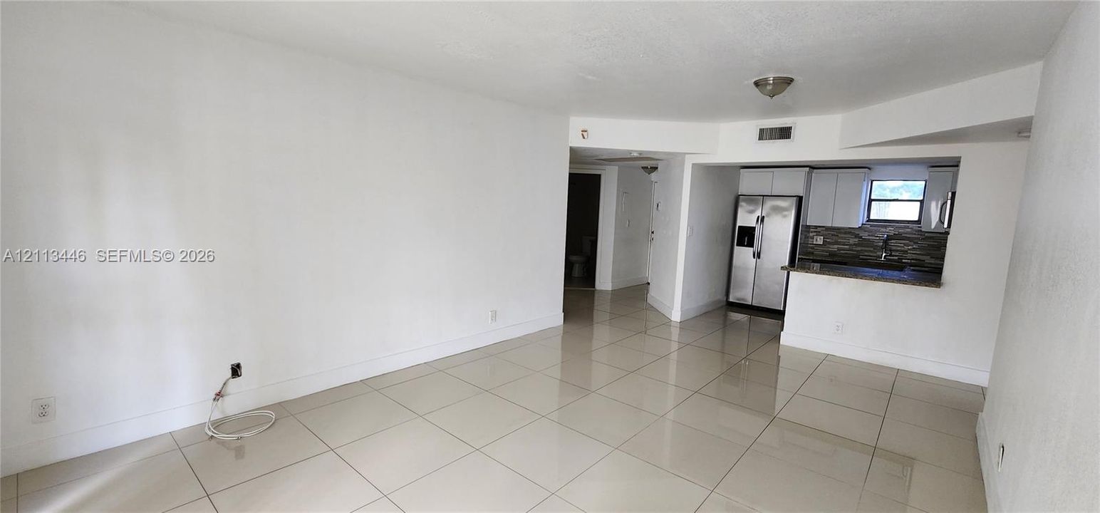 Large-format tile flooring, kitchen featuring stone countertops, stone-finish backsplash, stainless steel refrigerator, and shaker-style cabinetry