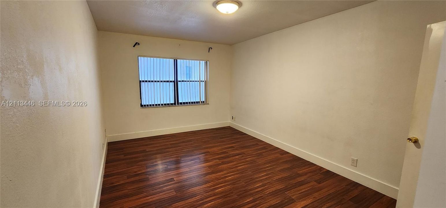 Room featuring wood-finish flooring, a flush-mount ceiling light fixture, and a window with vertical blinds