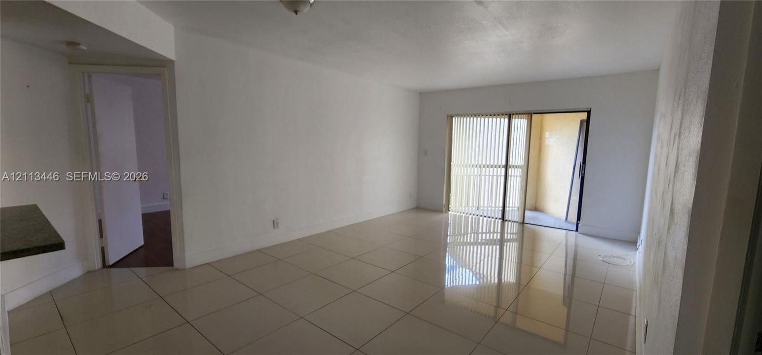 Open-concept interior featuring large-format tile flooring and sliding glass doors with vertical blinds