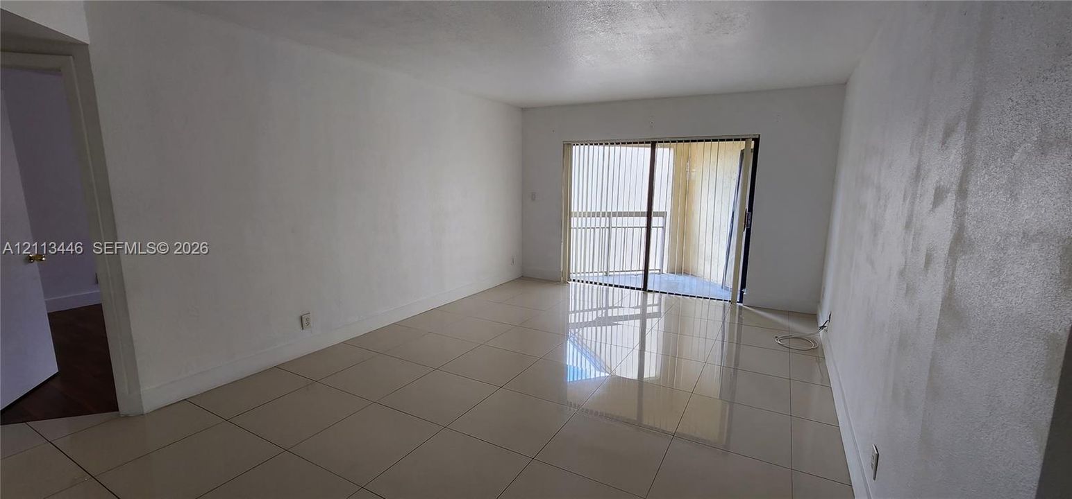 Open interior space featuring neutral wall tones, large-format tile flooring, and a sliding glass door providing external access