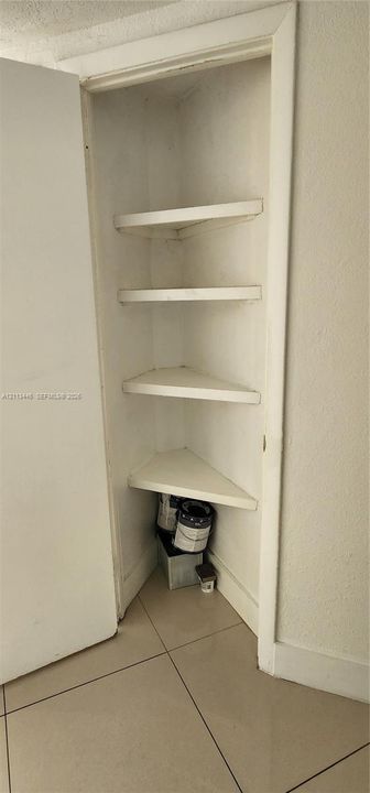 Built-in corner storage closet featuring four triangular shelving tiers and large-format tile flooring