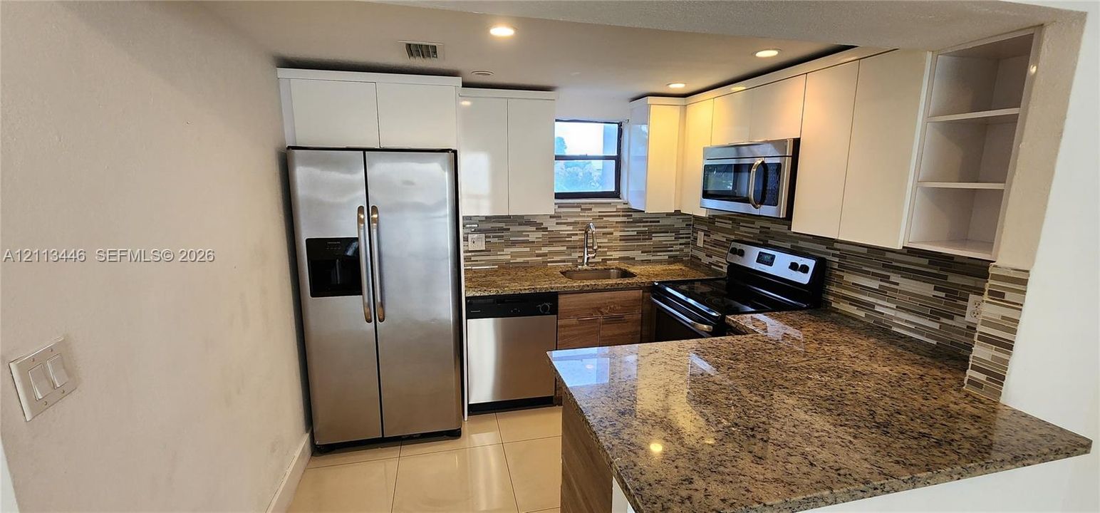 Kitchen featuring flat-panel white cabinetry, stone countertops, multi-toned mosaic tile backsplash, recessed lighting, and stainless steel appliances