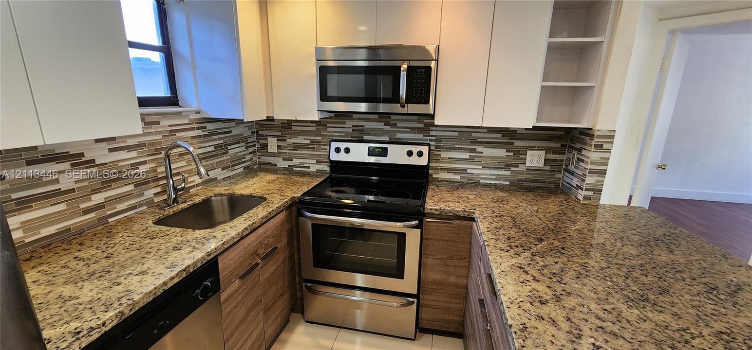 Kitchen featuring stone countertops, stainless steel appliances, white flat-panel cabinetry, a multi-tonal horizontal tile backsplash, and an undermount sink with a gooseneck faucet