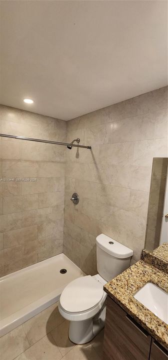 Bathroom featuring large-format wall tiling, a walk-in shower stall, a stone-finish countertop, an integrated sink, and recessed ceiling lighting