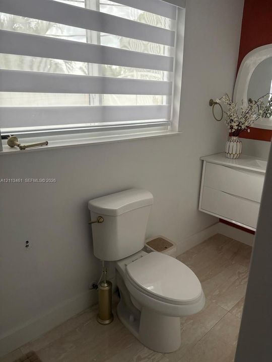 Floating white vanity with integrated basin, light-toned tiled flooring, adjustable horizontal window shade, and brushed metallic hardware