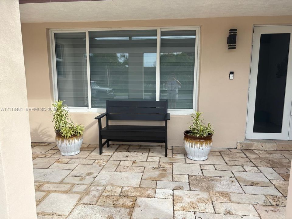 Covered entrance featuring stone paver flooring, a large multi-pane window with integrated blinds, and an exterior wall-mounted light fixture