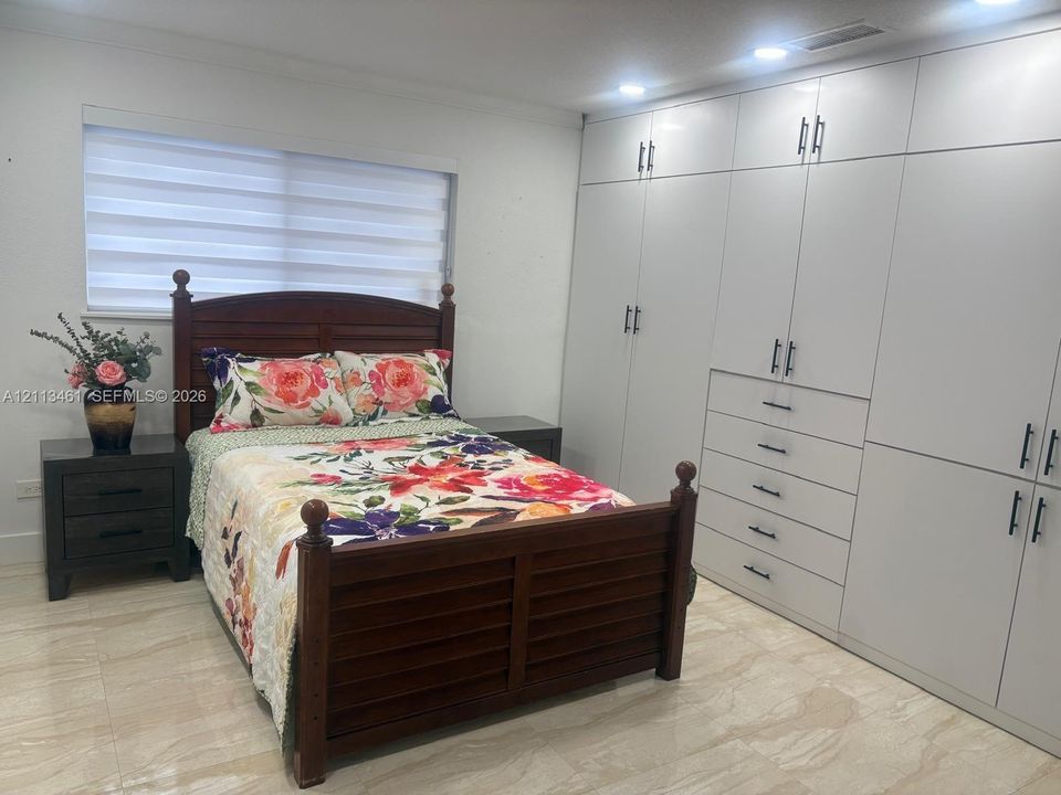Wall-to-wall built-in cabinetry featuring high-gloss white finish and matte black hardware, recessed ceiling lighting, and large-format tile flooring