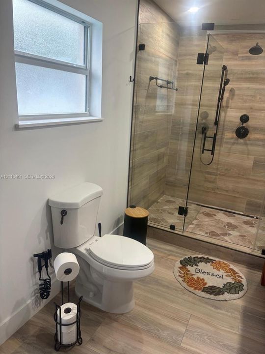Walk-in shower featuring glass enclosure, wood-finish wall tile, and matte black fixtures, paired with wood-finish flooring and privacy-glass window