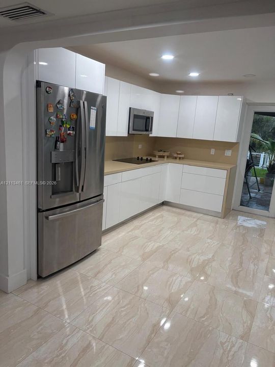 Kitchen featuring high-gloss white cabinetry, solid-surface countertops, stainless steel refrigerator and built-in microwave, and large-format tile flooring