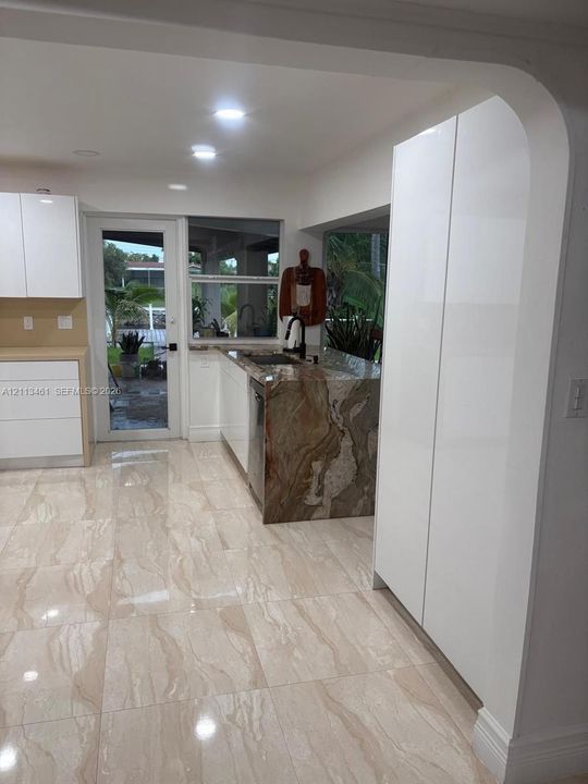 Kitchen featuring white slab-front cabinetry, stone-surface counters with a waterfall edge, large-format tile flooring, and a glass-paneled exterior door