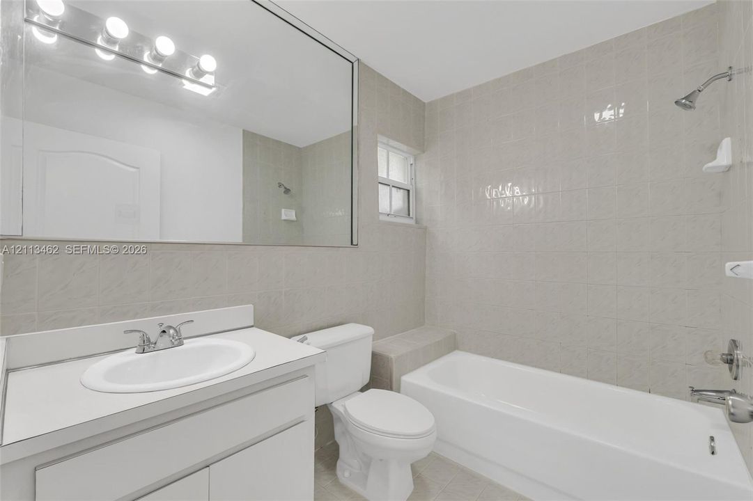 Bathroom featuring full-wall vanity mirror, white cabinet with integrated countertop sink, wall-mounted light fixture, and tile-surround shower and tub combination