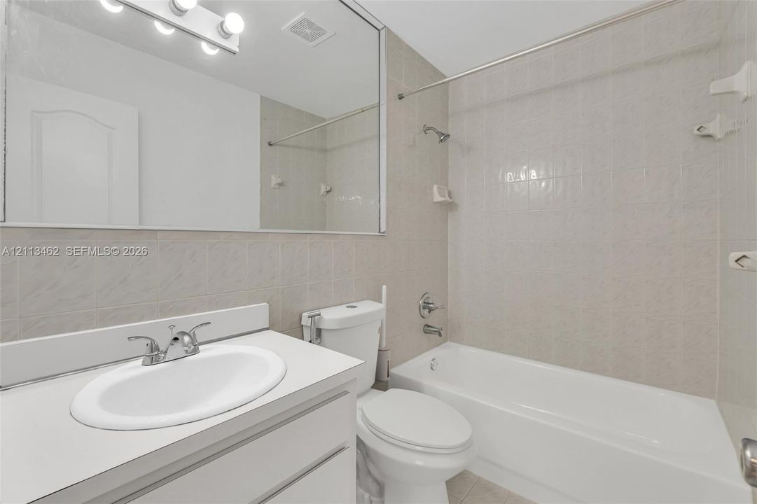 Bathroom featuring a vanity with a white countertop and oval under-mount sink, large wall-mounted mirror, overhead vanity lighting, and a shower-tub combination with ceramic tile surround