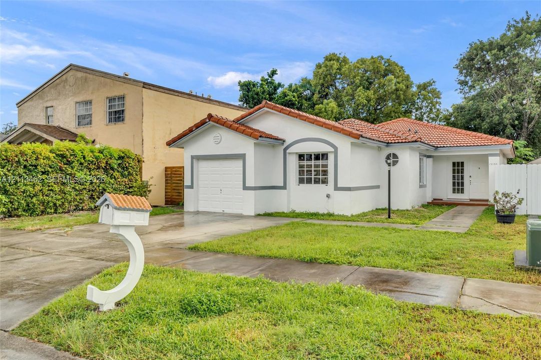 Stucco exterior featuring a terracotta tile roof, attached single-car garage, and custom curved mailbox
