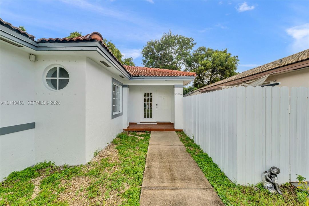 Exterior facade featuring stucco siding, red tile roofing, a circular accent window, and a white picket-style fence