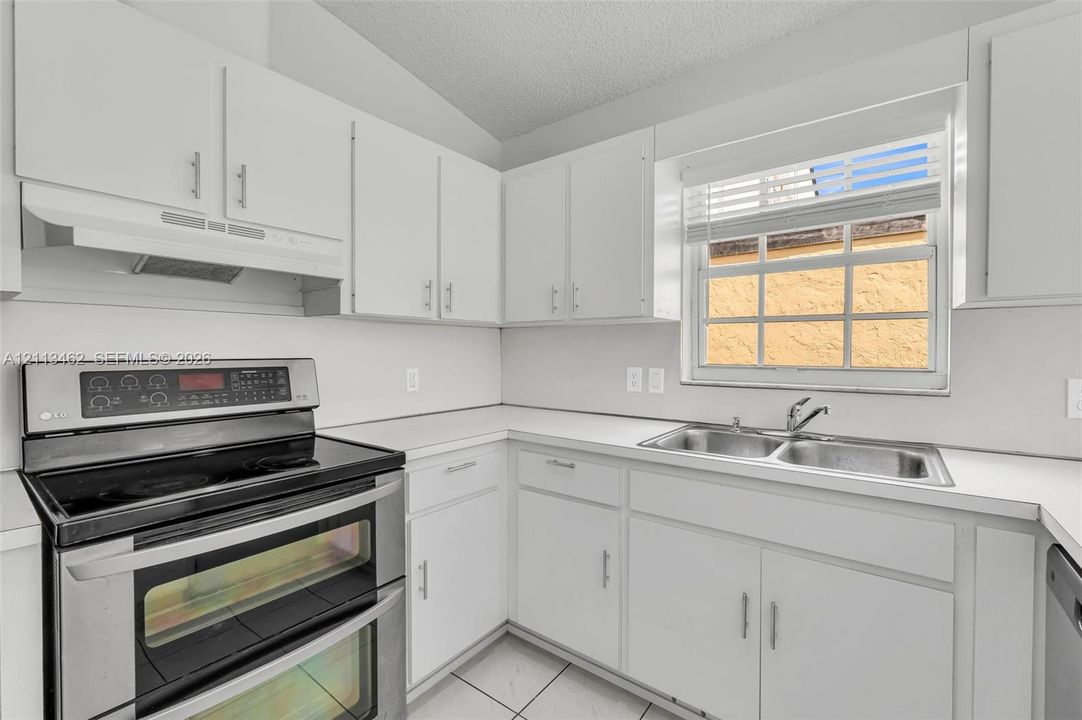 Kitchen featuring white cabinetry, solid-surface countertops, stainless steel double-oven range, integrated range hood, and double-basin stainless steel sink