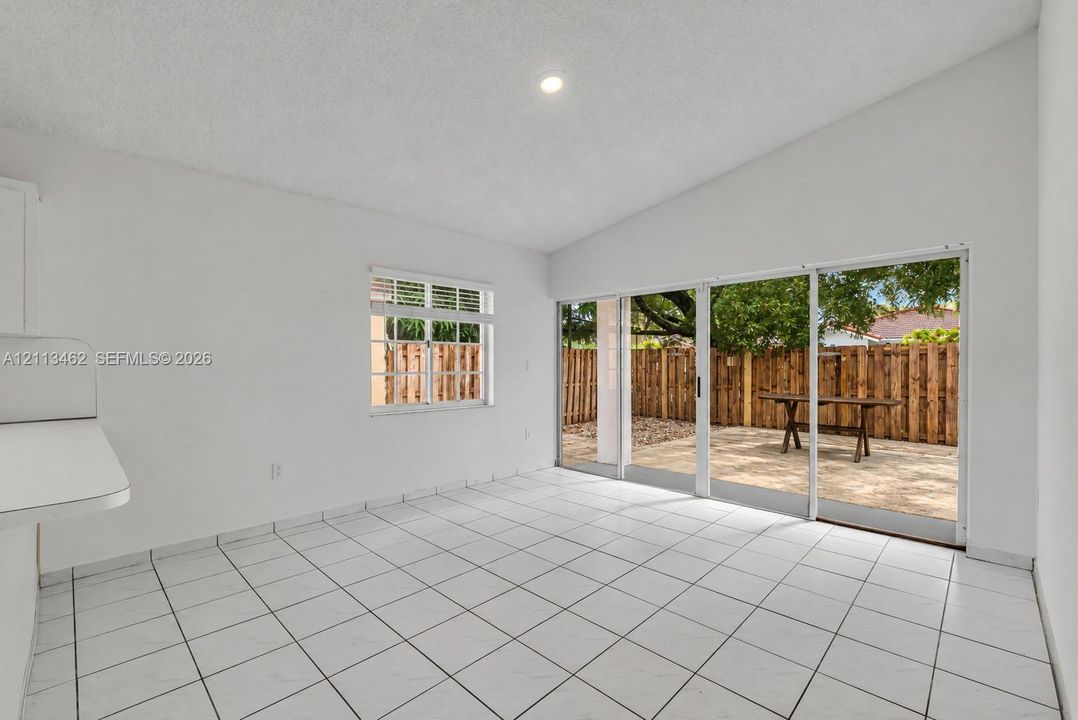 Room featuring white tile flooring, vaulted ceilings, recessed lighting, and large sliding glass doors providing outdoor access