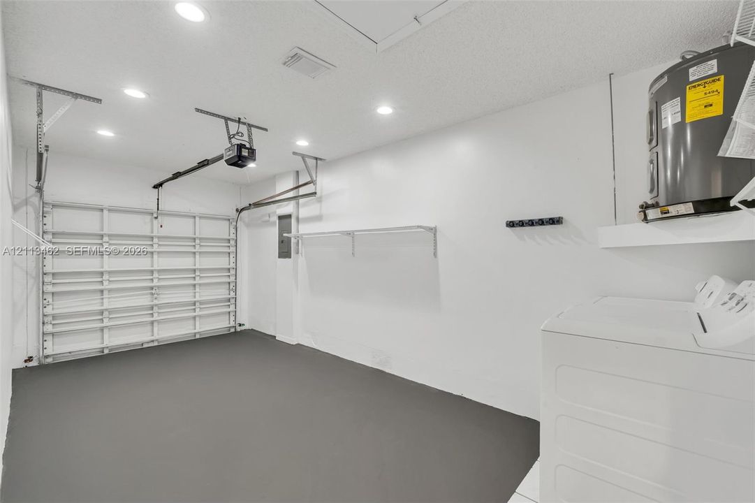 Finished garage featuring grey epoxy-coated flooring, recessed ceiling lighting, a metal garage door, and built-in wall-mounted shelving