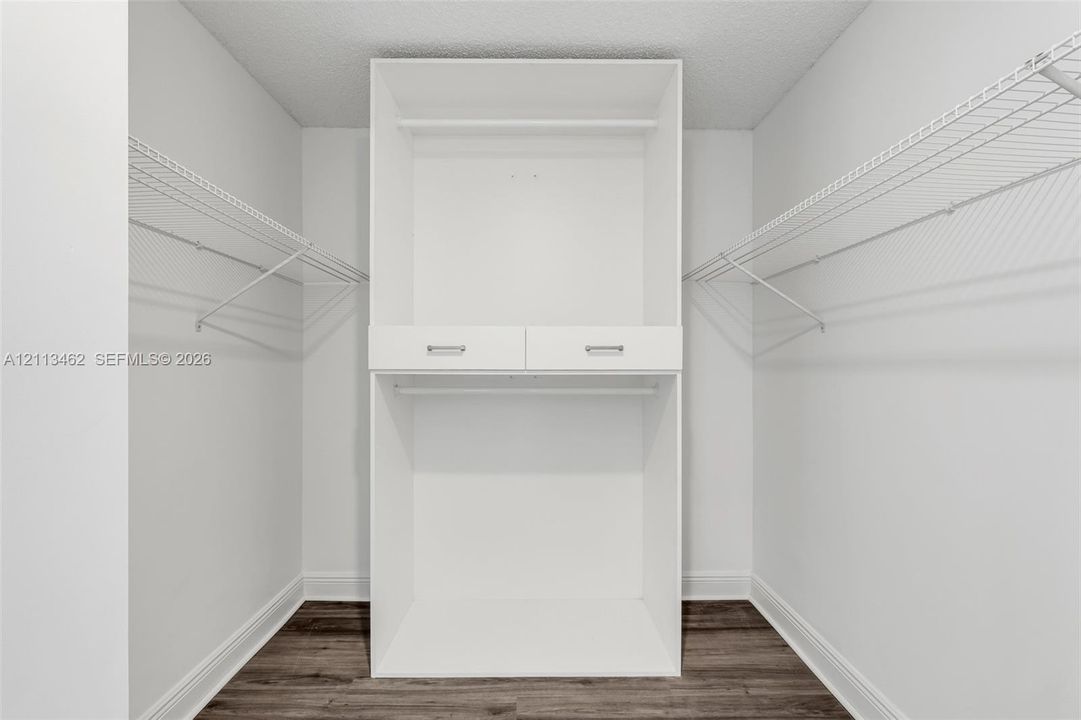 Storage closet featuring white built-in shelving, dual drawers with metal hardware, and dual-level wire racking, complemented by wood-finish flooring
