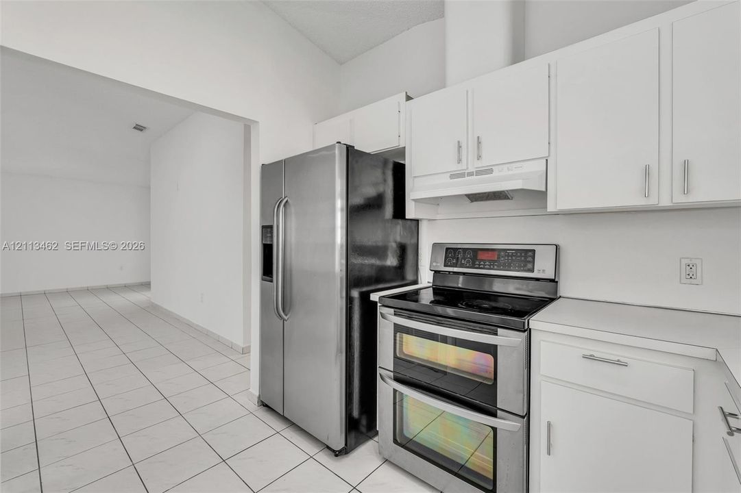 Kitchen featuring white cabinetry, stainless steel double-oven range, stainless steel refrigerator, and tile flooring