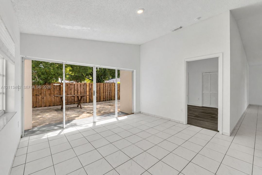 Open-concept room featuring white ceramic tile flooring, vaulted ceilings, recessed lighting, and multi-panel sliding glass doors providing access to a paved patio