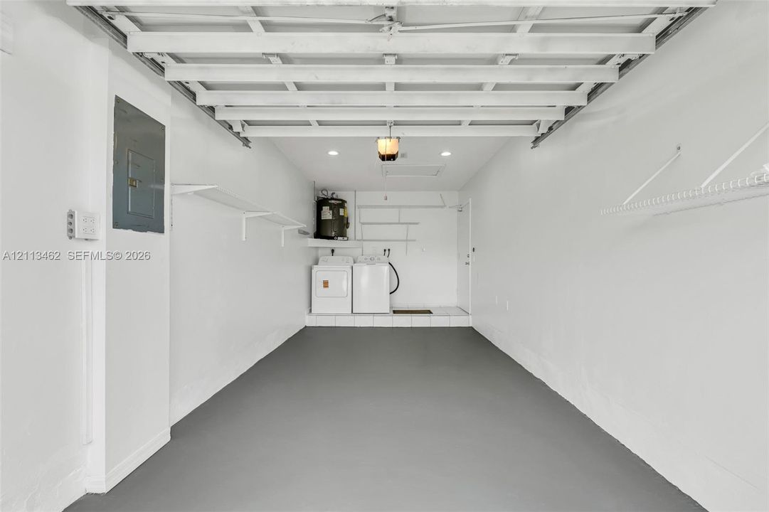 Finished interior space featuring epoxy-coated flooring, white walls, integrated wall-mounted shelving, recessed lighting, and a dedicated laundry area with water heater