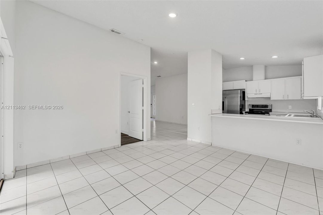 Open-concept interior featuring light-colored tile flooring, recessed lighting, breakfast bar, and stainless steel kitchen appliances