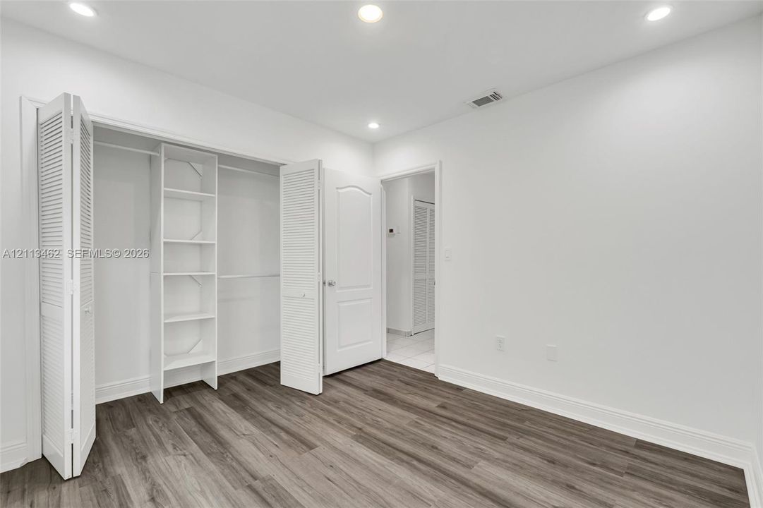 Wood-finish flooring, recessed lighting, and a reach-in closet with integrated shelving and louvered bifold doors