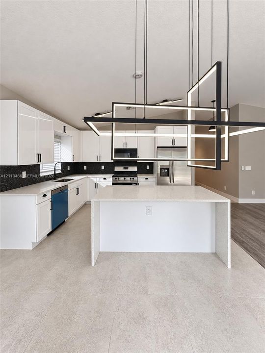 Kitchen featuring white shaker-style cabinetry, quartz countertops with a waterfall island, a dark tiled backsplash, and a linear geometric statement light fixture