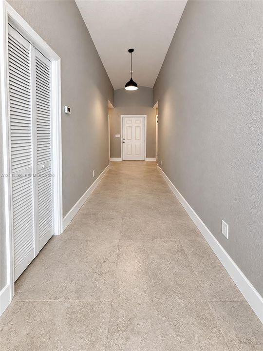 Hallway featuring neutral-tone ceramic tile flooring, louvered bi-fold closet doors, a vaulted ceiling, and a modern dome pendant light