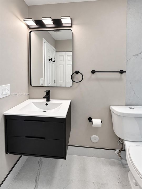 Floating vanity with matte black hardware, rectangular basin, contemporary three-light fixture, framed mirror, and coordinating matte black bathroom accessories