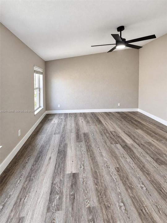 Room featuring slanted ceiling, wood-finish flooring, and a matte black ceiling fan with integrated lighting