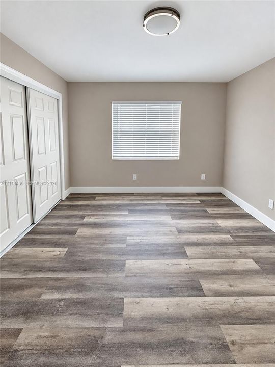 Room featuring wood-finish flooring, sliding panel closet doors, a centered flush-mount light fixture, and a window with horizontal blinds