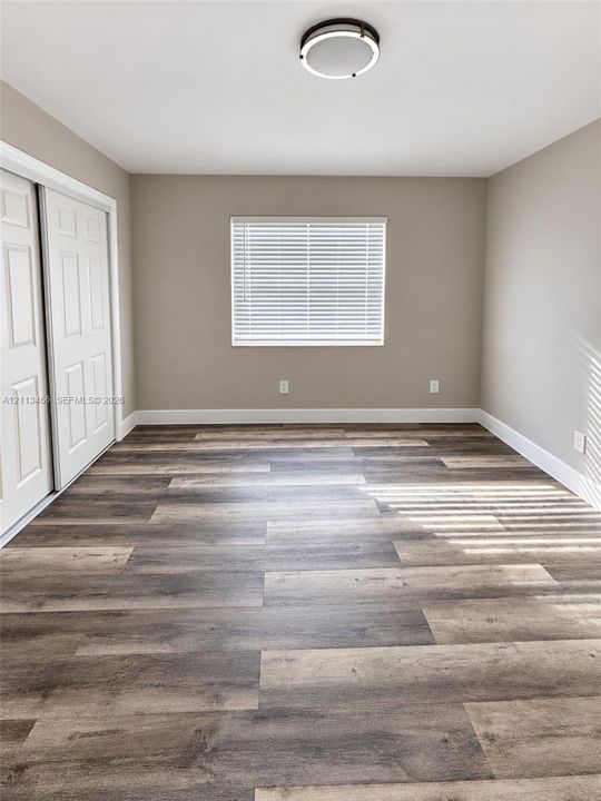 Room featuring wood-finish flooring, neutral wall paint, dual-panel sliding closet doors, and a central circular flush-mount light fixture