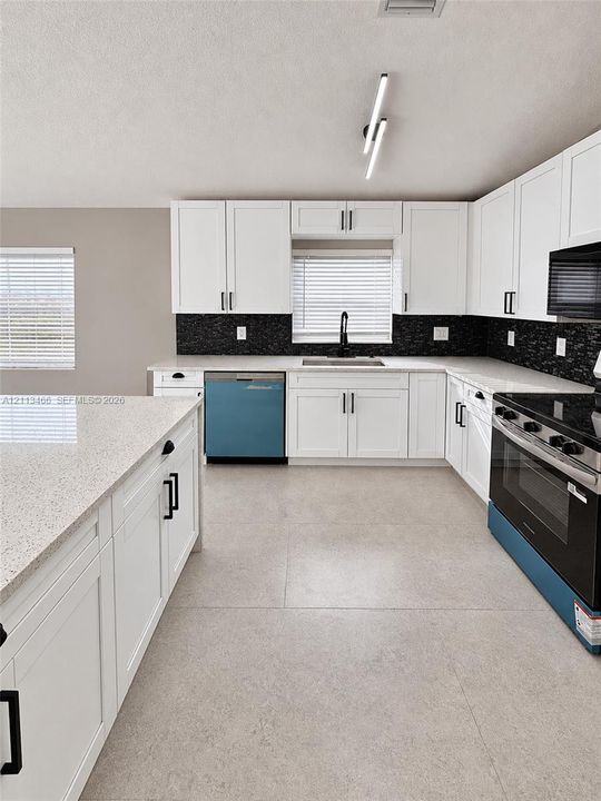Kitchen featuring white shaker-style cabinetry, quartz countertops, black tile backsplash, large-format neutral floor tile, and modern linear LED lighting