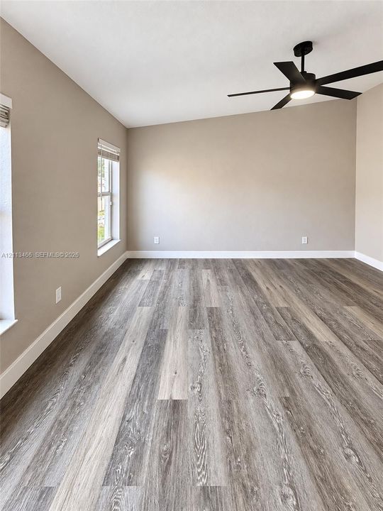 Room featuring wood-finish flooring, a matte black ceiling fan with integrated lighting, neutral wall paint, and multi-pane windows