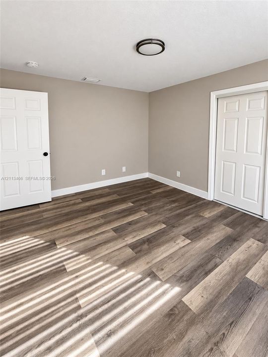 Neutral-toned walls paired with wood-finish flooring, featuring two white six-panel doors and a flush-mount circular ceiling light