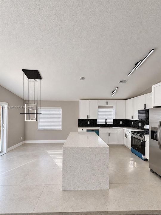 Kitchen featuring an expansive stone-surface island, white cabinetry, dark stone backsplash, large-format tile flooring, and contemporary pendant lighting