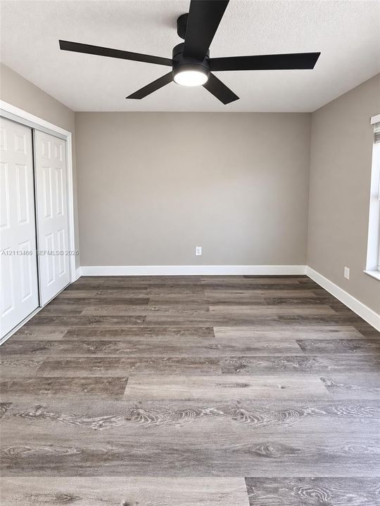 Wood-finish flooring, matte black ceiling fan with integrated lighting, and white sliding closet doors