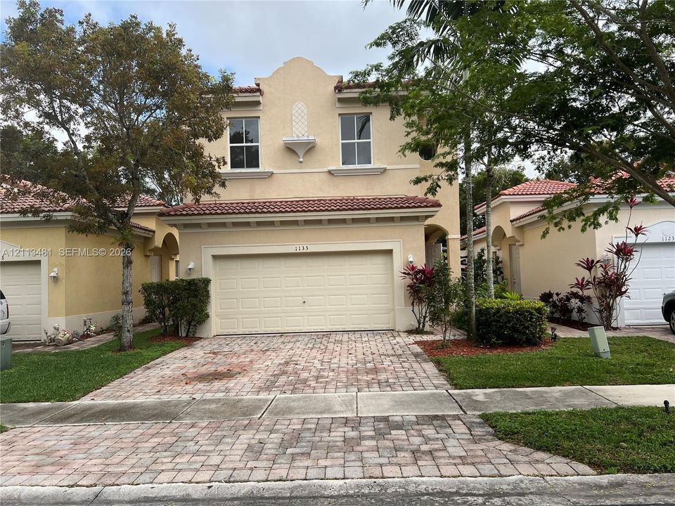 Stucco exterior featuring a decorative roofline, Spanish-style tile roof, attached two-car garage, and paver driveway