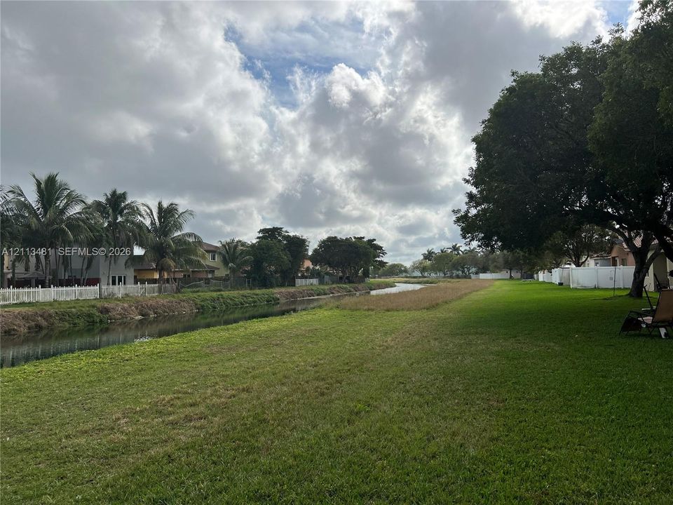 Expansive grassy lot featuring water frontage, mature trees, and perimeter fencing