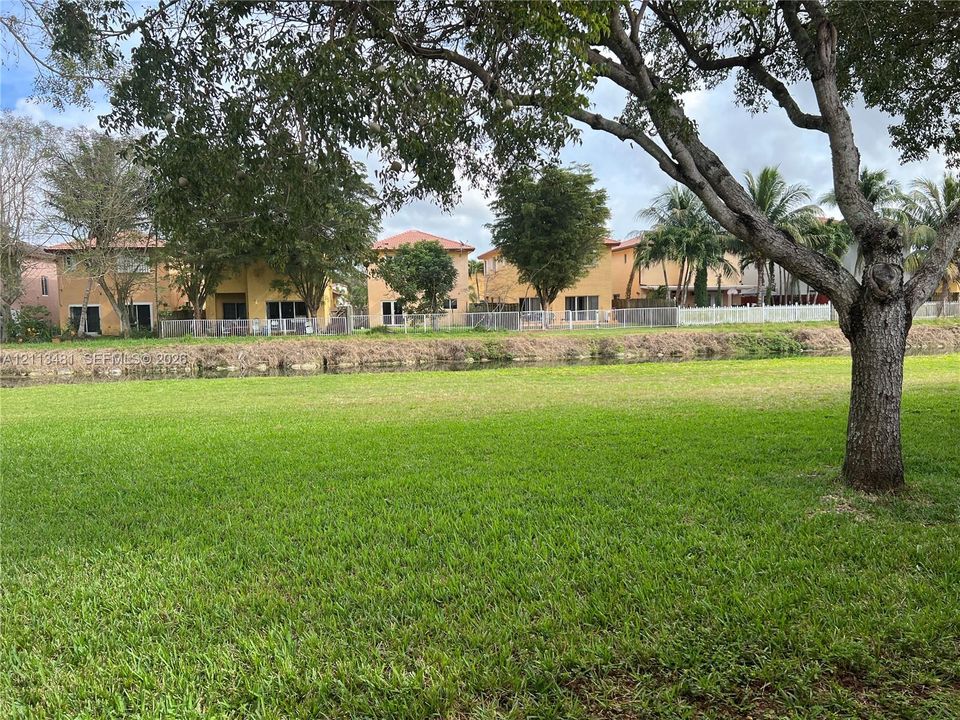 Expansive waterfront lawn featuring mature trees and a fenced perimeter