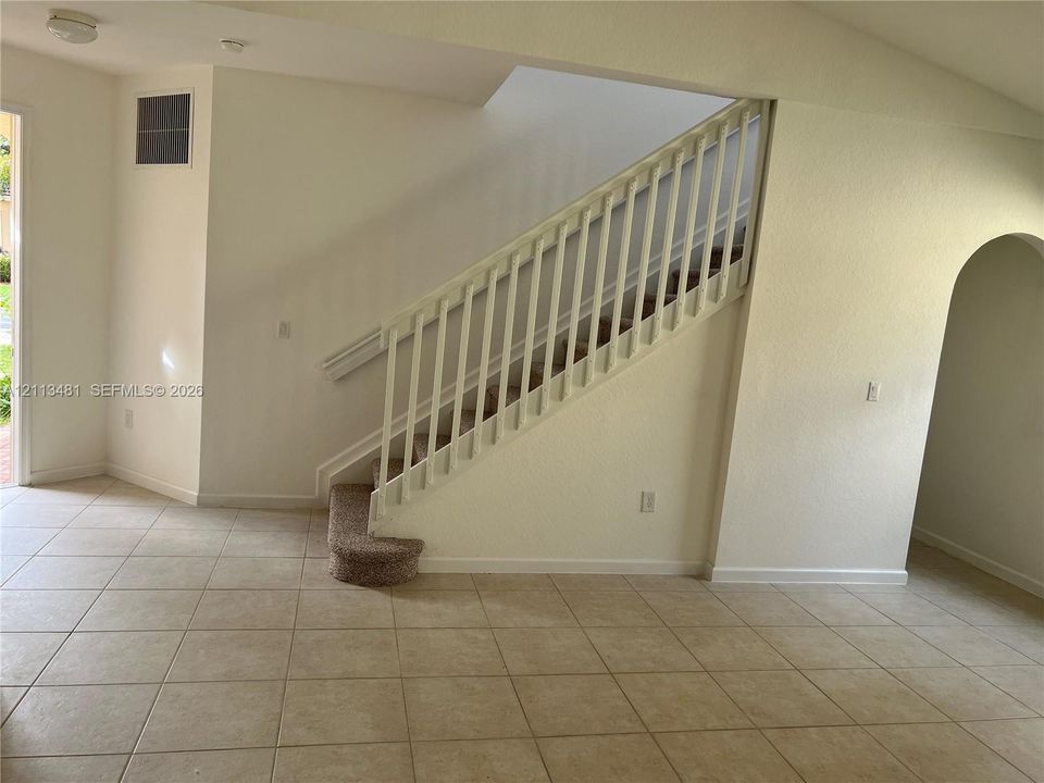 Staircase featuring a white balustrade, neutral carpeting, and a rounded bottom step, complemented by ceramic tile flooring and an arched entryway