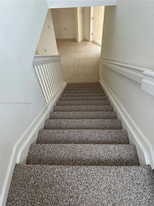 Staircase featuring neutral-tone carpeting, white painted handrails, and a white balustrade