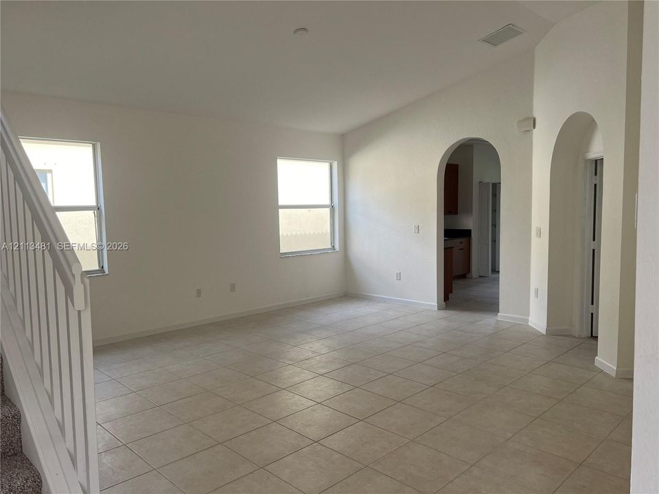 Open-concept interior featuring vaulted ceilings, neutral ceramic tile flooring, dual arched doorways, and a staircase with a white balustrade