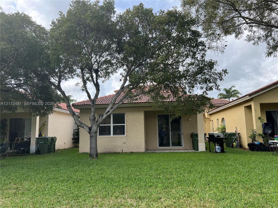 Stucco exterior featuring a tiled roof, sliding glass doors, and a lawn with mature trees