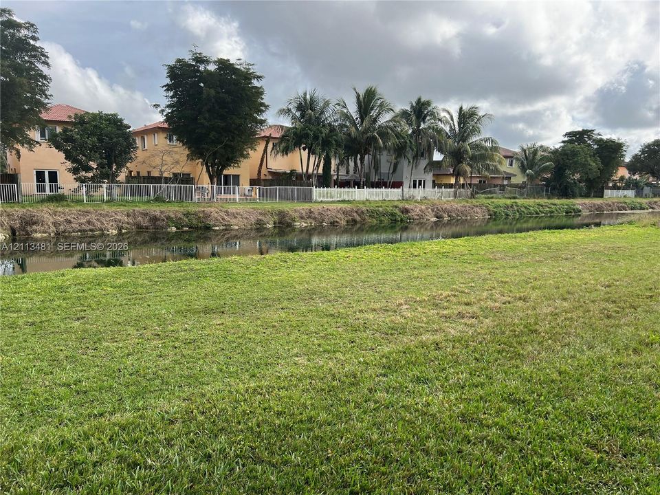 Expansive grassy lot featuring a canal border, white perimeter fencing, and mature palm trees