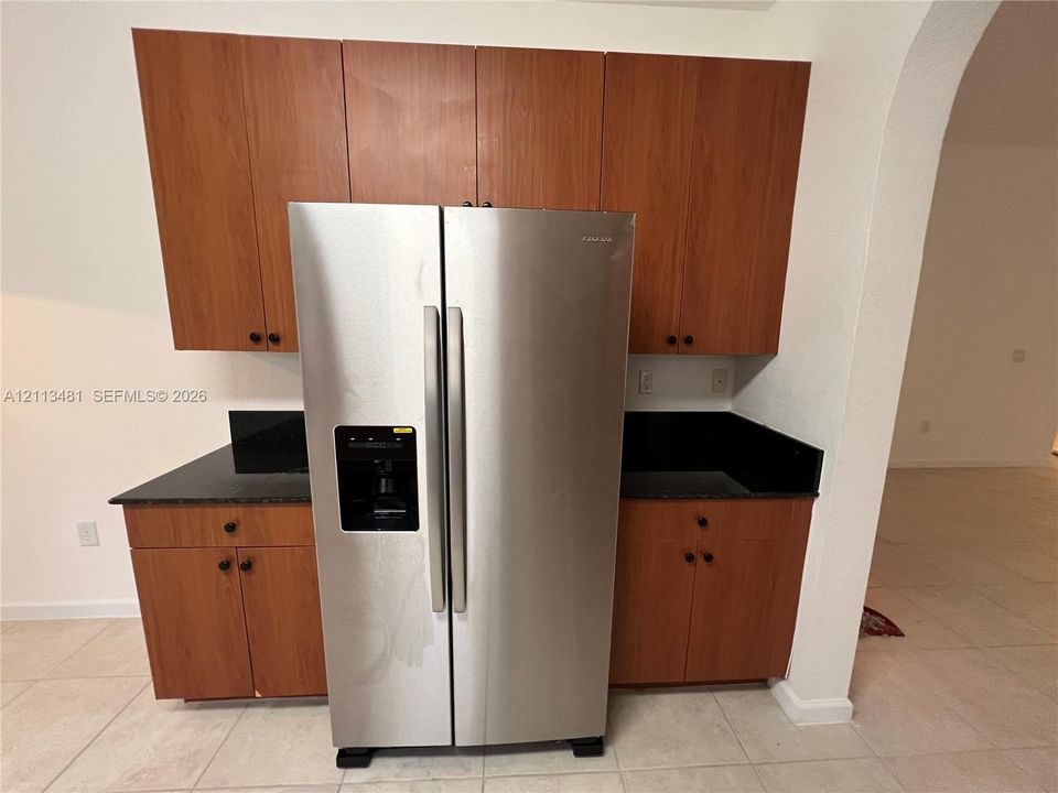 Kitchen cabinetry with wood-finish flat-panel doors, dark stone-surface countertops, and a side-by-side stainless steel refrigerator