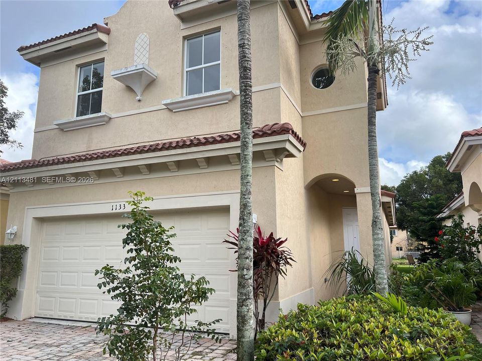 Stucco exterior featuring mission-style roof tiles, an arched entryway, decorative corbel details, and a paved driveway