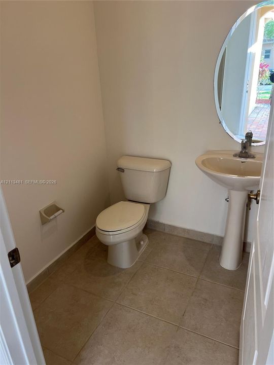 Powder room featuring tile flooring, pedestal sink, oval wall-mounted mirror, and standard-height toilet